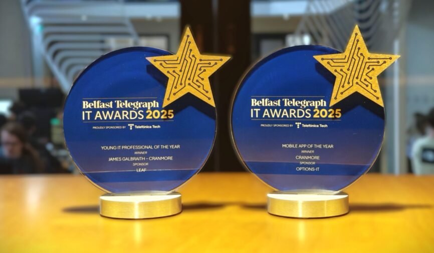 Two blue Belfast Telegraph IT Award trophies on a desk. One for Mobile App of the Year and the other for Young IT Professional of the Year.
